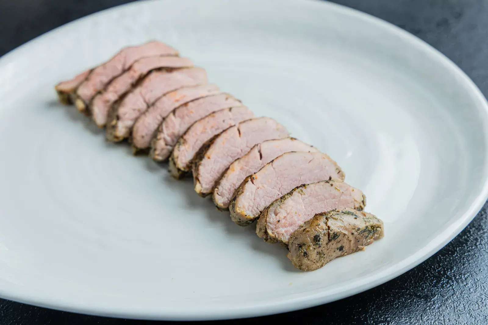 Close-up of sous-vide pork tenderloin slices showing the even pink centre and peppered crust